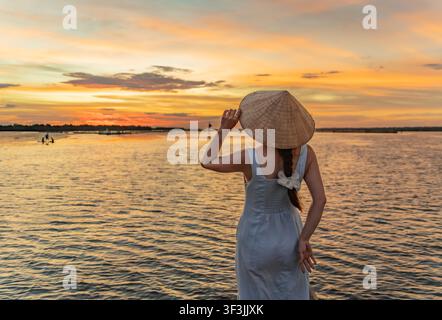 Frau mit einem Kegelhut beobachtet den Sonnenuntergang, Tam Giang-Lagune, Hue, Vietnam Stockfoto