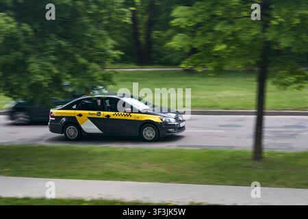 Minsk, Belarus - 28. Mai 2021: Volkswagen Polo Limousine in Yandex Go Taxi-Bemalung fährt schnell auf der Stadtstraße an grünen Parkbäumen vorbei, aufgenommen mit Schwenkpanoramat Stockfoto