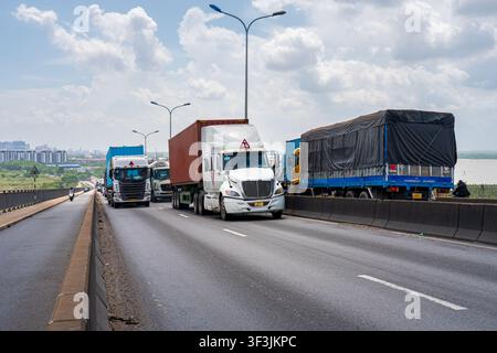 Lastwagen fahren über die Phu-My-Brücke über den Saigon-Fluss, mit der Skyline von Ho-Chi-Minh-Stadt und dramatischen Wolken im Hintergrund. Stockfoto