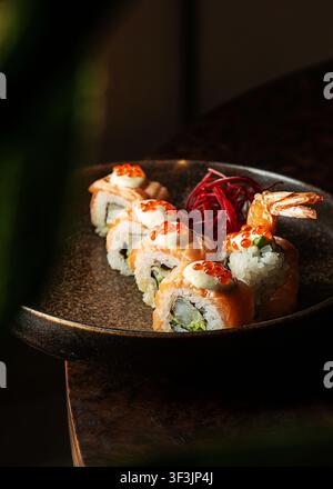 Nahaufnahme eines professionellen Fotos von Gourmet-Sang-Uramaki-Rollen mit cremiger Sauce und Ikura-Kaviar, garniert mit gebratenem Garnelen Schwanz und geriebener Stockfoto