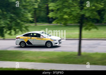 Minsk, Belarus - 28. Mai 2021: Hyundai Solaris Limousine, Markenwagen des Yandex-Taxidienstes, fährt im Sommer an grünen Parkbäumen auf einer asphaltierten Stadtstraße vorbei wit Stockfoto
