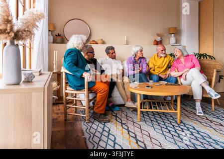 Verschiedene Gruppe von älteren Freunden, die zusammen sitzen, kommunizieren und soziale Zeit in einem komfortablen Wohnzimmer genießen, was Gemeinschaft und Gesundheit fördert Stockfoto