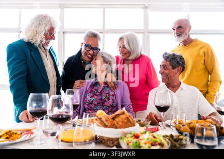 Gruppe verschiedener älterer Freunde, die lachend und gemeinsam eine Mahlzeit zu Hause genießen, die Zeit miteinander verbringen und während eines festlichen Treffens die Freundschaft feiern Stockfoto