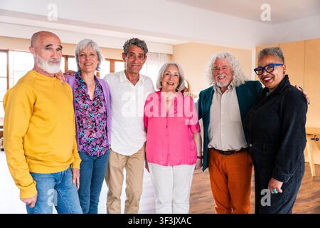 Gruppe glücklicher, verschiedener Seniorenfreunde, die sich umarmen und in die Kamera lächeln, und die dauerhafte Freundschaft, den Ruhestand und die Gemeinschaft in einem einladenden Stockfoto