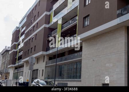 Ein zeitgenössisches mehrstöckiges Wohnhaus mit Balkonen und großen Fenstern steht entlang einer städtischen Straße. Die Szene zeigt moderne Wohnarchitektur Stockfoto