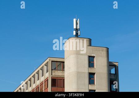 Mobilfunk-Basisstationantennen, die auf dem Dach eines modernen Betongebäudes in Tessin montiert sind. Niedrigwinkelaufnahme des Mobilfunkmastes Stockfoto
