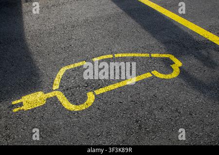 Gelbfarbenes elektrisches Auto-Symbol auf schwarzem Asphaltboden, das einen reservierten EV-Ladestell-Parkplatz markiert. Hochwinklige Nahaufnahme der Straßenoberfläche Stockfoto