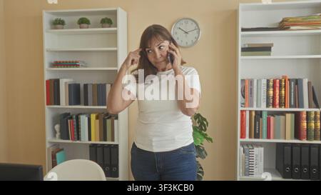 Frau, die das Smartphone hält, zeigt den Finger auf den Tempel, während sie im Gebäude telefoniert; durchdachte Problemlösung. Stockfoto