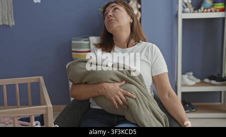 Frau, die ein eingewickeltes Baby und eine Flasche hält, Kopf nach hinten geneigt in einem Gebäude-Kinderzimmer; Müdigkeit Fürsorge Trost. Stockfoto