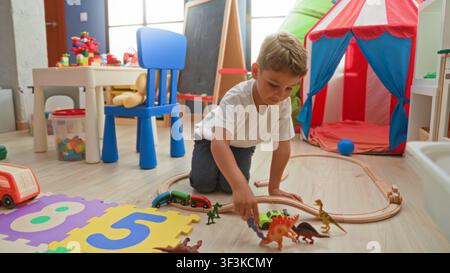 Junge kniet und greift mit der Hand nach einer Spielzeugbahn auf dem Holzboden in einem Gebäude-Spielzimmer mit Zelt, Stuhl und Schaumstoff-Puzzleteppich; fantasievolles Spielvergnügen. Stockfoto