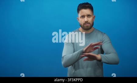Mann mit Bart und sichtbaren Händen zuckt mit den Handflächen nach oben und erhobenen Augenbrauen vor einem nahtlosen blauen Studio-Hintergrund; Unsicherheit. Stockfoto