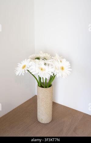 Weiße Gerbera-Tulpenblumen in Keramikvase auf Holztisch mit minimaler Inneneinrichtung Stockfoto