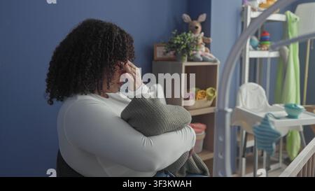 Die Frau wiegt das Baby in eine graue Decke, reibt die Augen und legt den Kopf neben dem Kinderbett mit einem gefüllten Häschen an die blaue Wand im Gebäude; Erschöpfungströst. Stockfoto