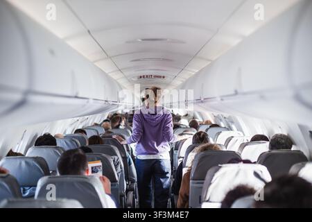 Innenraum des Flugzeugs mit Passagieren auf Sitzen und weiblichen Reisenden, die den Gang gehen. Kommerzielles Economy-Flugdienstkonzept Stockfoto