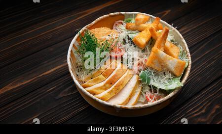 Gegrilltes Hühnchensalat Caesar mit Parmesan, knusprigen Croutons, Kirschtomaten und Microgreens in einer rustikalen Schüssel auf dunklem Holzuntergrund, frisch und hea Stockfoto