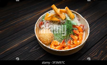 Gegrillte Garnelen-Cäsar-Salat mit Parmesan, knusprigen Croutons, geballtem Käse, Kirschtomaten und Mikrogrün in einer rustikalen Schüssel auf dunklem Holz-Hintergrund Stockfoto