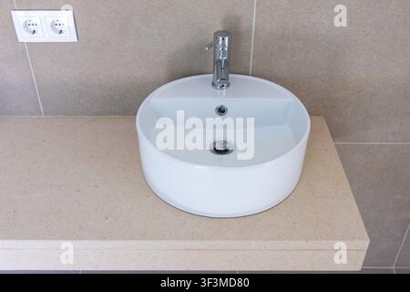 Ein sauberes und zeitgemäßes Badezimmer-Setup mit einem runden Keramikwaschbecken und einem eleganten Metallwasserhahn, der auf einer gesprenkelten Steinoberfläche montiert ist Stockfoto