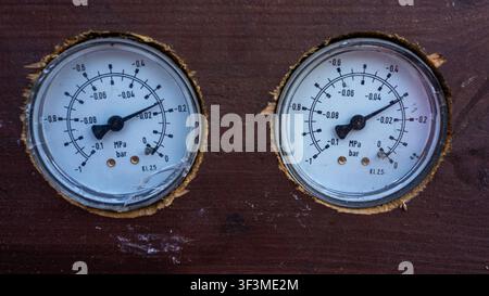 Zwei Vintage-Druckmessgeräte, die auf verwittertem Holz montiert sind. Die Zifferblätter zeigen Messwerte mit abgenutzten Kanten und verblassten Markierungen. Rost und Schmutz deuten auf langfristigen Gebrauch hin Stockfoto