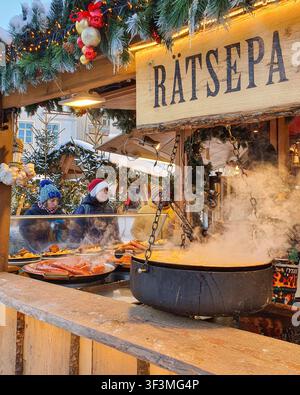 Tallinn, Estland - 7. Jan. 2024: Händler kochen Würste in einem großen Topf an einem Weihnachtsmarkt-Stand. Stockfoto