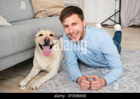 Junger glücklicher Kerl, der mit seinem Hund auf dem Boden liegt Stockfoto