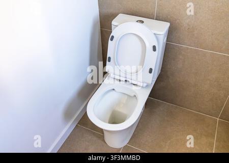 Eine zeitgenössische Keramiktoilette und ein Spülkasten stehen auf einem Fliesenboden neben einer schlichten weißen Wand Stockfoto