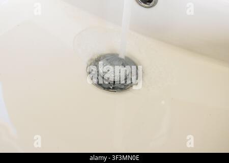 Nahaufnahme von Wasser, das wirbelt und durch einen Chrom-Abflusssieb in einem Keramikwaschbecken abfließt Stockfoto