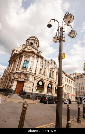 Niedrigwinklige Ansicht, die nach oben auf das New Oxford House an der Ecke Waterloo Street und Bennetts Hill im Stadtzentrum von Birmingham, West Midlands, England, zeigt, fotografiert am 6. Mai 2012. Das klassische Steingebäude verfügt über einen markanten Eck-Uhrturm mit Kuppel, ionische Säulen der Rieserordnung und gewölbte Erdgeschossfenster. Ein dekorativer Straßenlaternenpfosten mit mehreren Laternen steht im Vordergrund an der Kopfsteinpflaster-Eckstraße, mit geparkten Autos entlang des Bordsteins unter einem bewölkten Himmel. Stockfoto