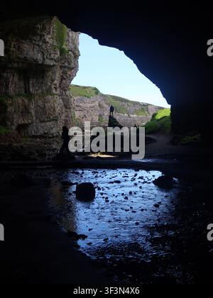 Eine Ansicht aus der großen äußeren Höhle der Smoo-Höhle, die durch Meerwassererosion gebildet wurde, mit Blick auf den blauen Himmel und die Küste von Sutherland. Stockfoto