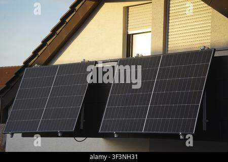 Eine Dachgeschosswohnung mit einem Balkon und großen Solarpaneelen. Die Abendsonne scheint noch mit goldenem Licht auf die Fenster und die Balkontür, aber die Stockfoto