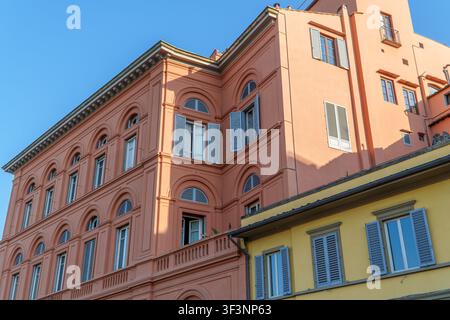 Sonnenlicht beleuchtet schöne pfirsichfarbene und gelbe historische Gebäude mit offenen Fensterläden vor einem lebendigen klaren blauen Himmel in Italien. Stockfoto