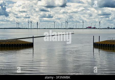 Windturbinen an einer fernen Küste, die nachhaltige Energie produzieren, mit Wellenbrechern und einem Industriegebiet, das die Szene ergänzt Stockfoto