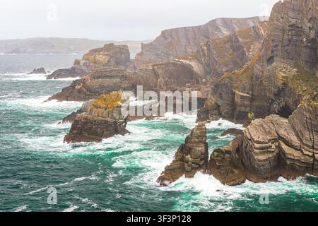 Panoramablick auf schroffe Seeklippen am Wild Atlantic Way in Irland. Mächtige türkisfarbene Wellen des Atlantischen Ozeans schlagen gegen geschichtete Felsen für Stockfoto