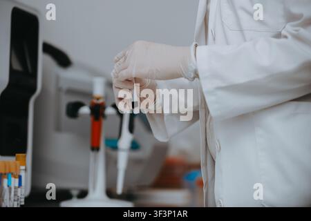 Wissenschaftler in weißem Laborkittel hält Reagenzglasprobe mit Pipetten und medizinischer Ausrüstung im Labor Stockfoto