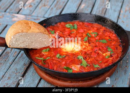 Traditionelle Shakshuka mit pochierten Eiern in würziger Tomatensauce, serviert in einer Gusseisenpfanne mit frischem Brot Stockfoto