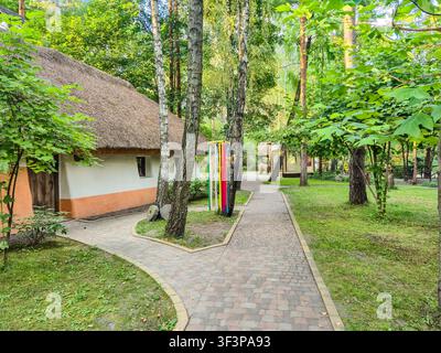 Ein malerischer Weg führt durch einen üppigen grünen Park und präsentiert authentische ukrainische ländliche Architektur und historische Artefakte Stockfoto