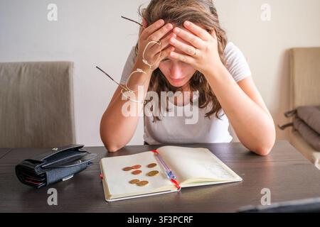 Frau, die zu Hause mit finanziellen Problemen kämpft, Münzen zählt, gestresst ist und Kopfschmerzen hat Stockfoto