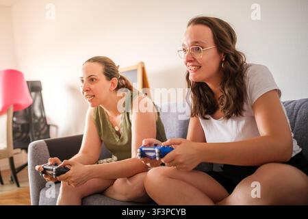Zwei fröhliche Frauen genießen Videospiele zusammen, während sie auf einer Couch sitzen Stockfoto