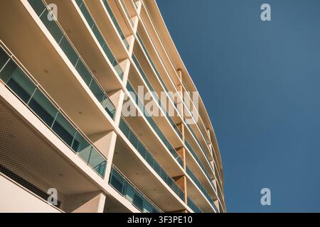 Zeitgenössisches Wohnhaus mit geschwungenen Balkonen und Glasgeländern vor einem klaren blauen Himmel Stockfoto