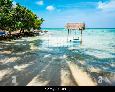Pittoreske Barakuda Beach mit einer rustikalen Holzschaukel über klarem, flachem, türkisblauem Wasser neben üppigen grünen Bäumen, die einen entspannenden Urlaubsort schaffen Stockfoto
