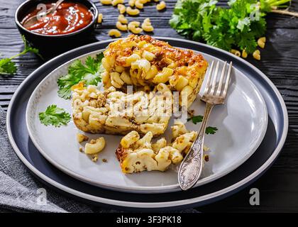 Traditionelle amerikanische Hausgemachte Gebackene Hackfleisch-Mac-and-Cheese-Auflauf mit goldener Kruste und zarten Nudelscheiben auf einem Teller auf schwarzem Holztisch Stockfoto