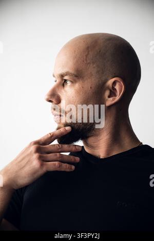 Mann, der mit der Hand am Kinn in einem einfachen Hintergrund am Tag nachdenkt Stockfoto