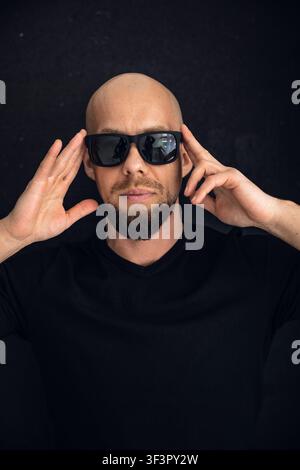 Mann mit Sonnenbrille posiert mit den Händen am Kopf in einem dunklen Raum während eines Fotoshootings Stockfoto