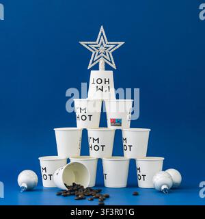 Kreative Komposition von Kaffeetassen, die wie ein Weihnachtsbaum gestapelt sind, mit silbernem Stern auf blauem Hintergrund. Weihnachts- und Neujahrskonzept. Stockfoto