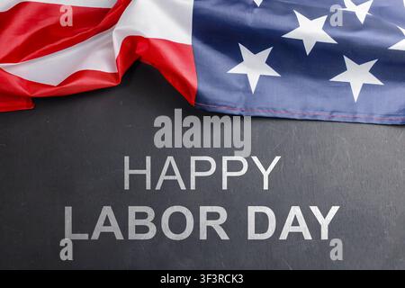 Glückliche Labor-Day-Textnachricht, die auf einem schwarzen Holzbrett mit Hintergrund der amerikanischen Flagge geschrieben ist. Hochwertiges Foto Stockfoto