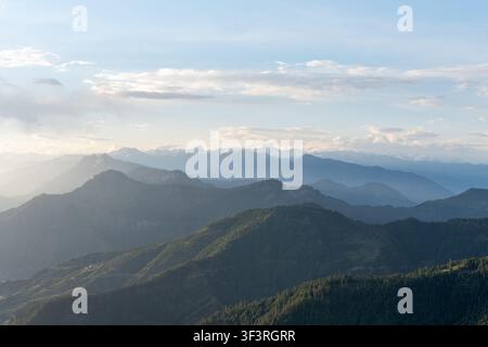Eine breite horizontale Landschaftsansicht von geschichteten Bergkämmen, entfernten schneebedeckten Dhauladhar-Gipfeln unter einer bewölkten Himmelsdecke in Himachal Pradesh, Indien. Stockfoto