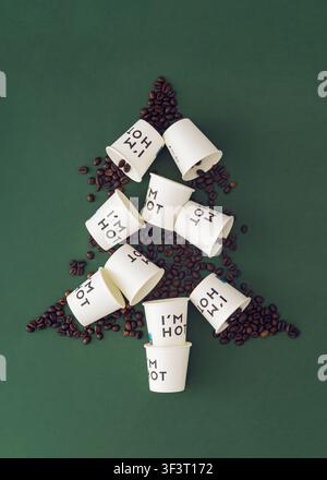 Weihnachtsbaum aus Papp-Kaffeebechern zum Mitnehmen und Kaffeebohnen auf grünem Hintergrund. Kreatives Weihnachts- und Neujahrskonzept. Festlicher Feiertags-Flachlay Stockfoto