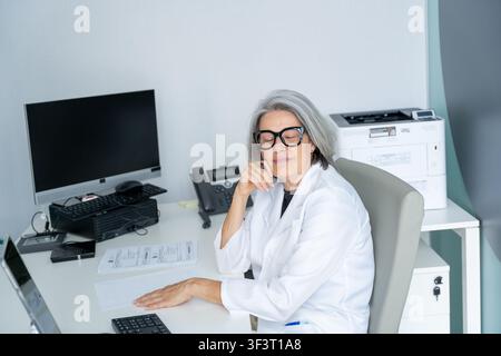 Erfahrene weibliche Gesundheitsfachkraft sitzt mit geschlossenen Augen in Gedanken an einem Schreibtisch Stockfoto