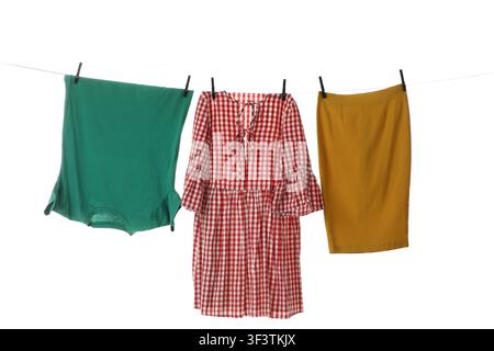Grünes T-Shirt, rotes Gingham-Kleid und gelber Rock, die mit Wäscheklammern an einer Wäscheleine hängen, isoliert Stockfoto