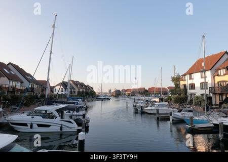 Mehrere Yachten, die an Häusern im Hythe Marina Village an einem sonnigen Tag festgemacht sind, mit dem Southampton Cruise Terminal im Hintergrund Stockfoto