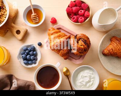 Ein köstliches Frühstücksbufet mit flockigen Croissants, frischen Himbeeren und Blaubeeren, cremigem Joghurt, einer Tasse Kaffee, Orangensaft und Honig Stockfoto